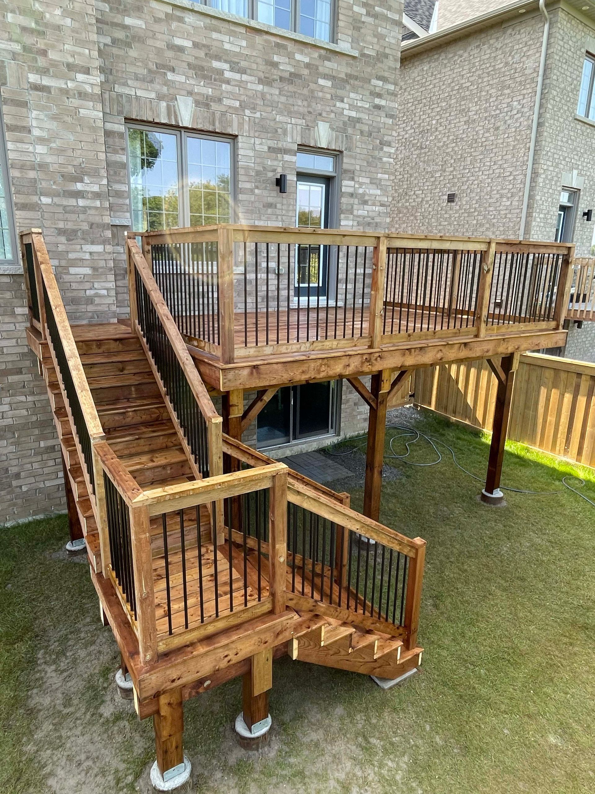 A wooden deck with stairs leading up to it is in the backyard of a house.