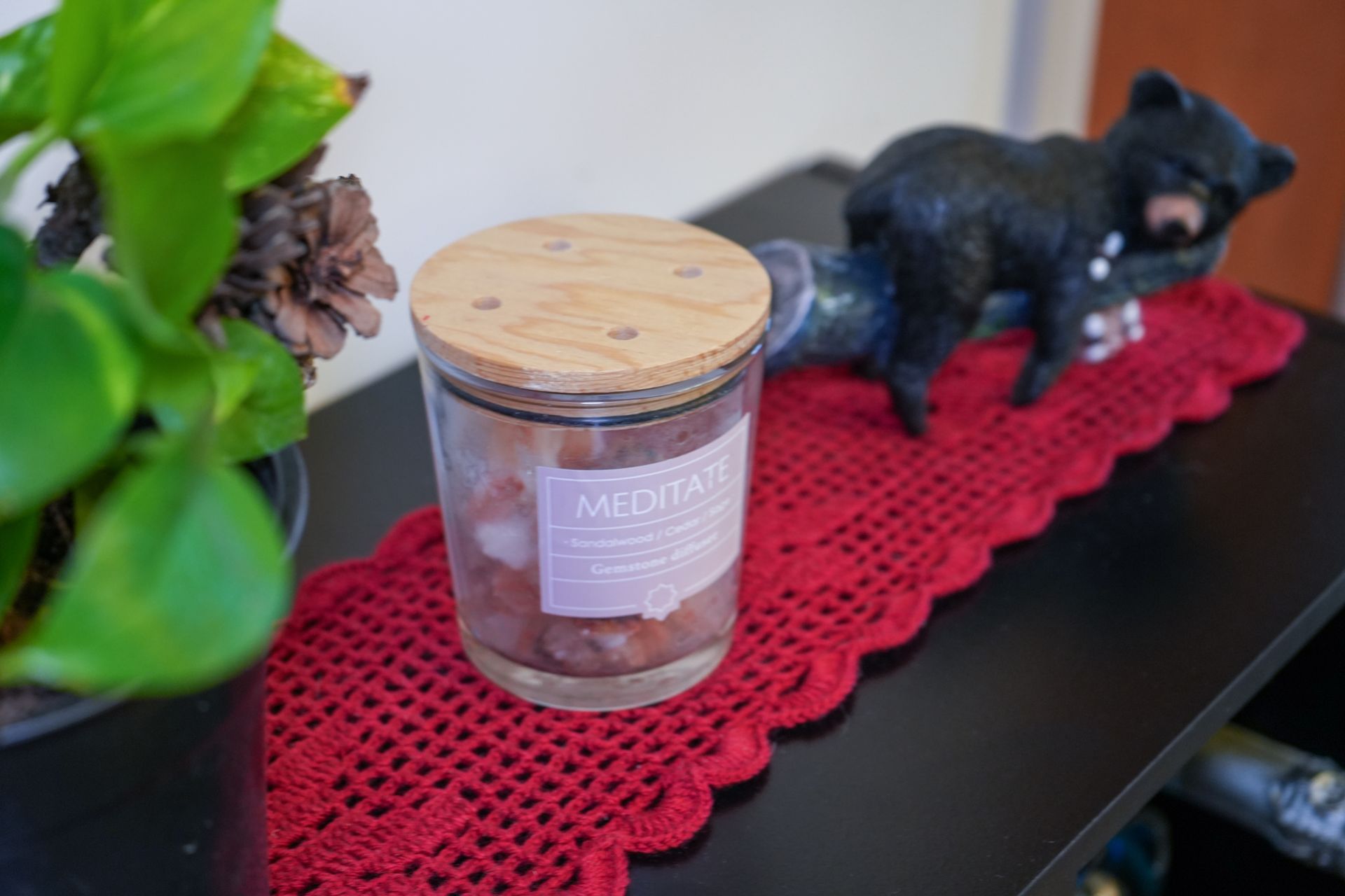 A candle in a glass jar with a wooden lid is sitting on a table next to a plant.