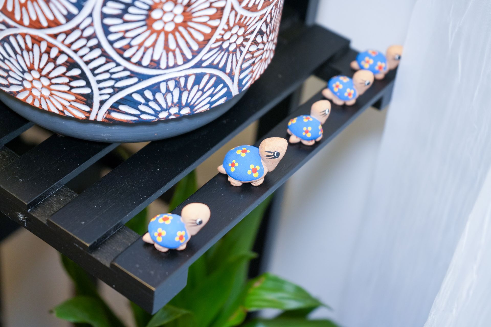 A row of small turtles are sitting on a shelf next to a plant.