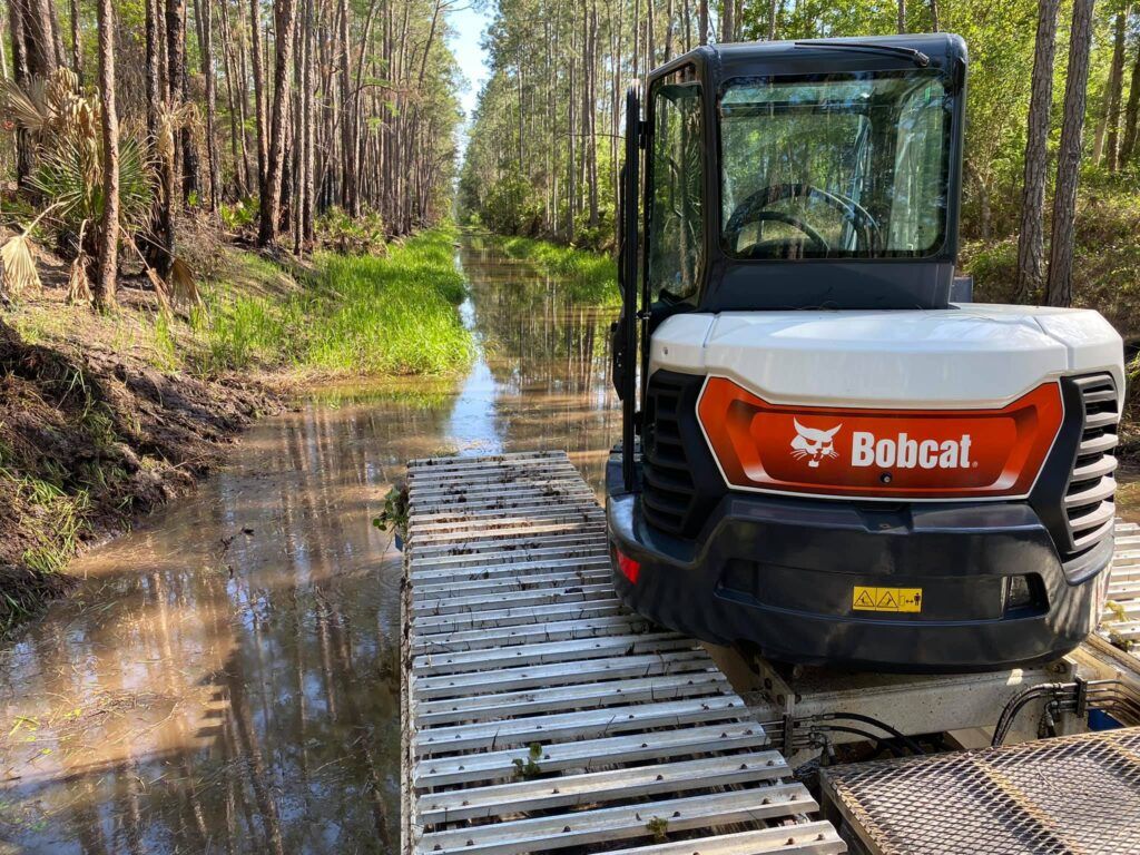 A bobcat excavator is driving through a muddy river.