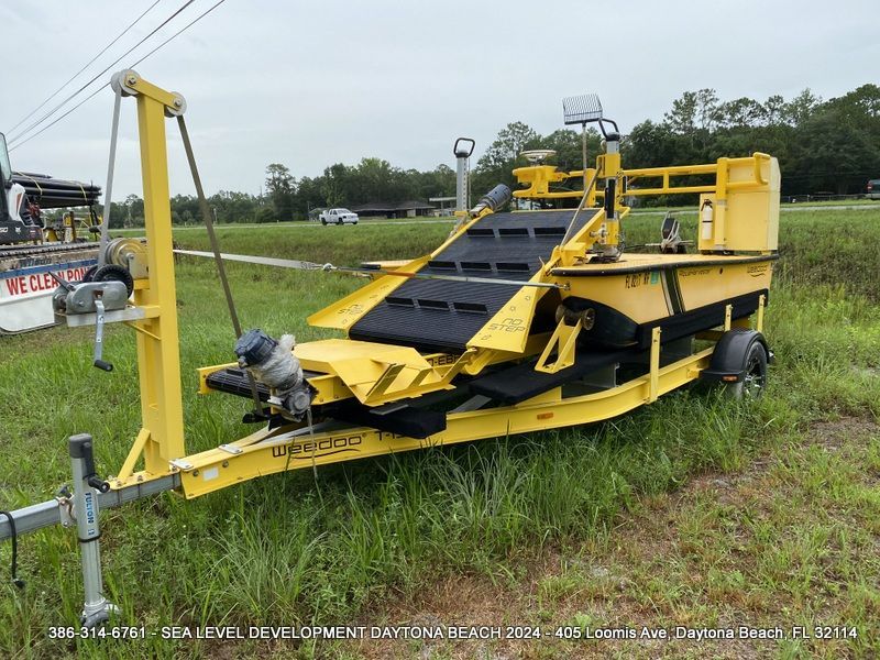 A yellow Weedoo trailer is parked in a grassy field.