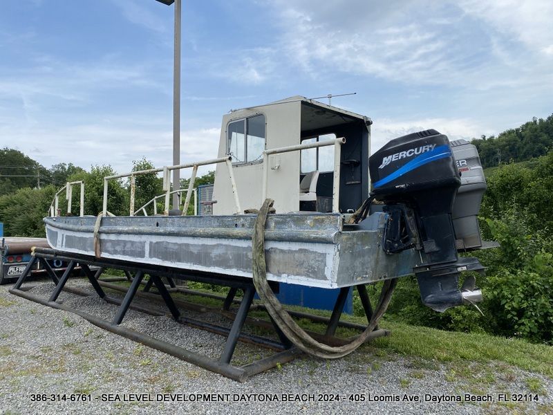 A boat with a mercury outboard motor is parked on a gravel road.