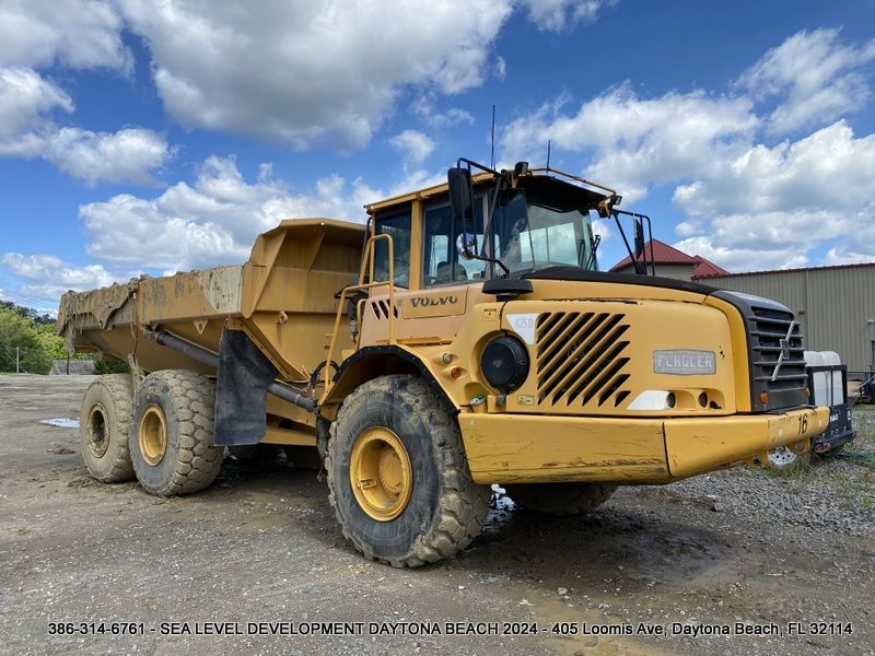 A large yellow dump truck is parked in a dirt lot.