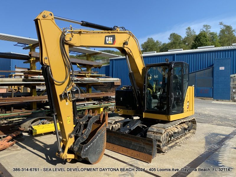 A yellow cat excavator is parked in front of a blue building