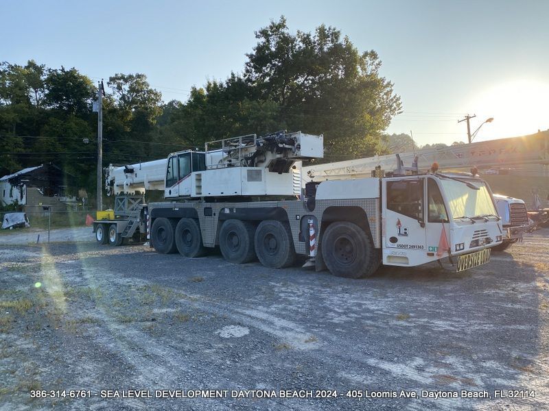 A large white crane is parked in a gravel lot.