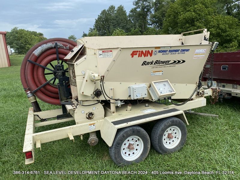 A finn trailer with a hose attached to it is parked in a grassy field.