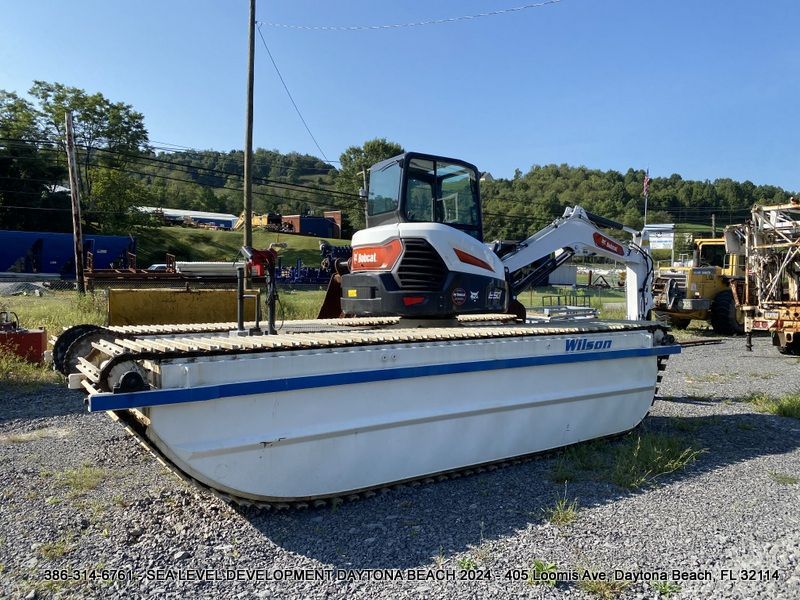 An amphibious tracked  bobcat excavator is sitting on top of a boat in a gravel lot in Daytona Beach in Volusia County, FL.