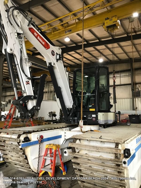 A bobcat excavator is sitting on top of a truck in a garage.