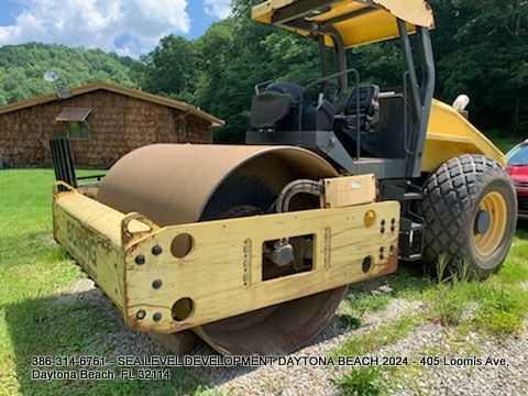 A yellow and black road roller is parked in a grassy field.