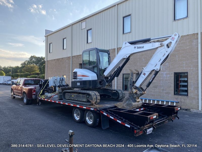 A bobcat excavator is on a flatbed trailer in front of a building.