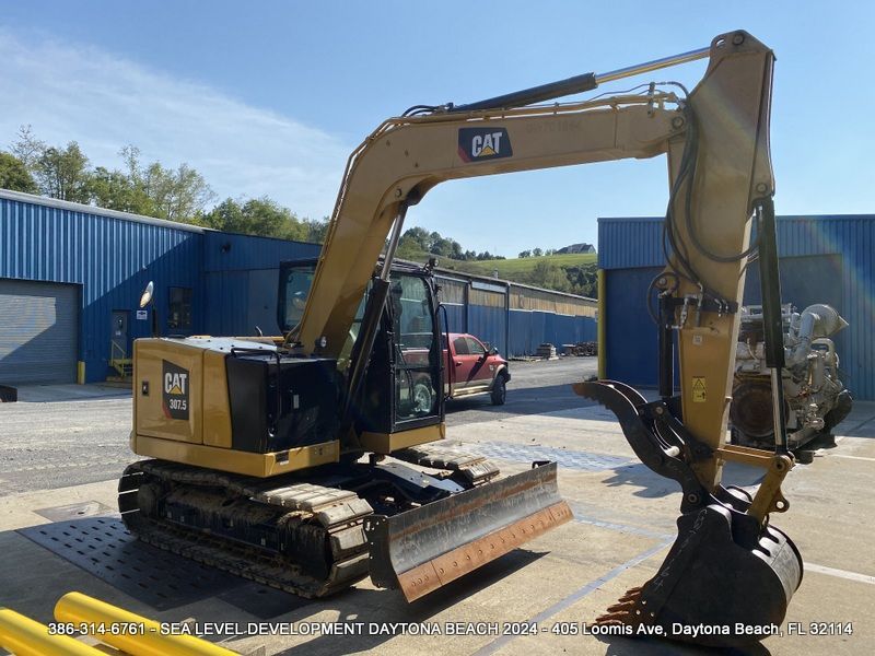 A cat excavator is parked in front of a blue building