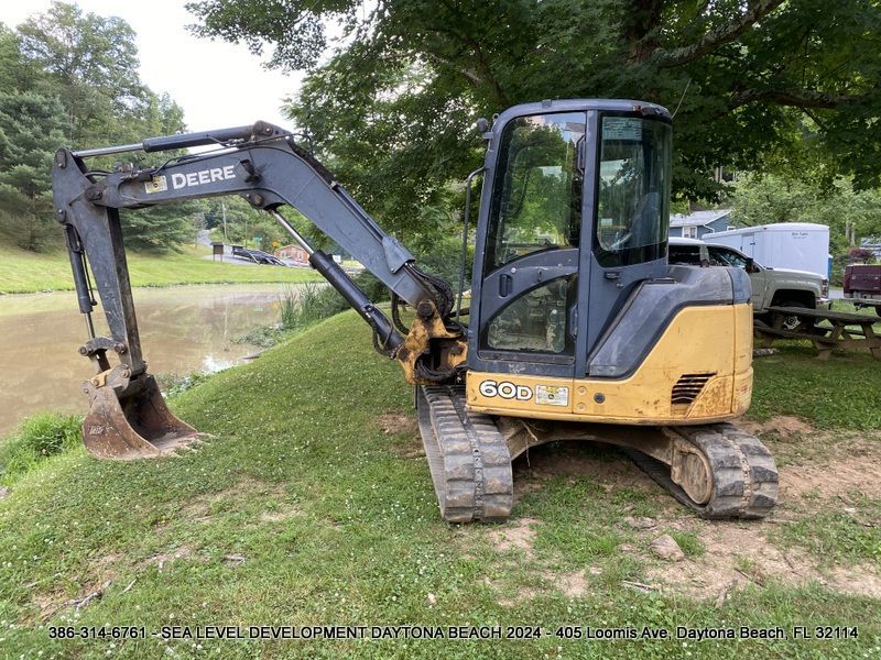 A small excavator is parked on a grassy hill next to a body of water.