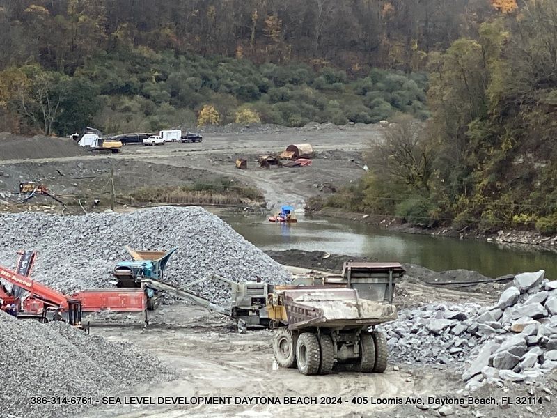 A large dump truck is driving down a dirt road next to a river