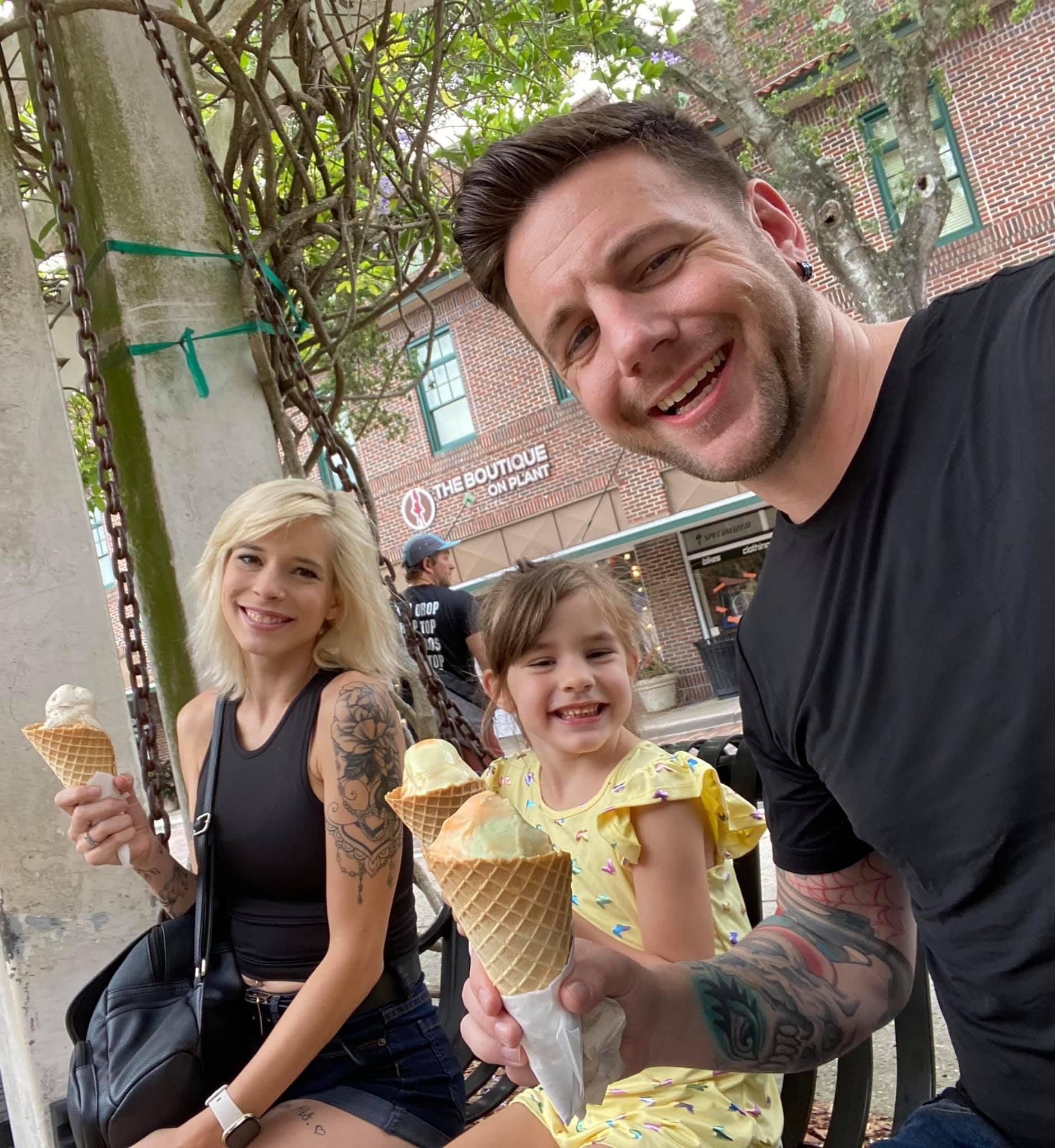 Family enjoys ice cream cones outdoors; man, woman, child smiling.