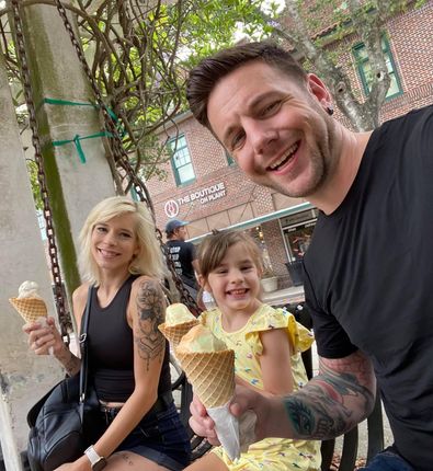 Family enjoys ice cream cones outdoors; man, woman, child smiling.