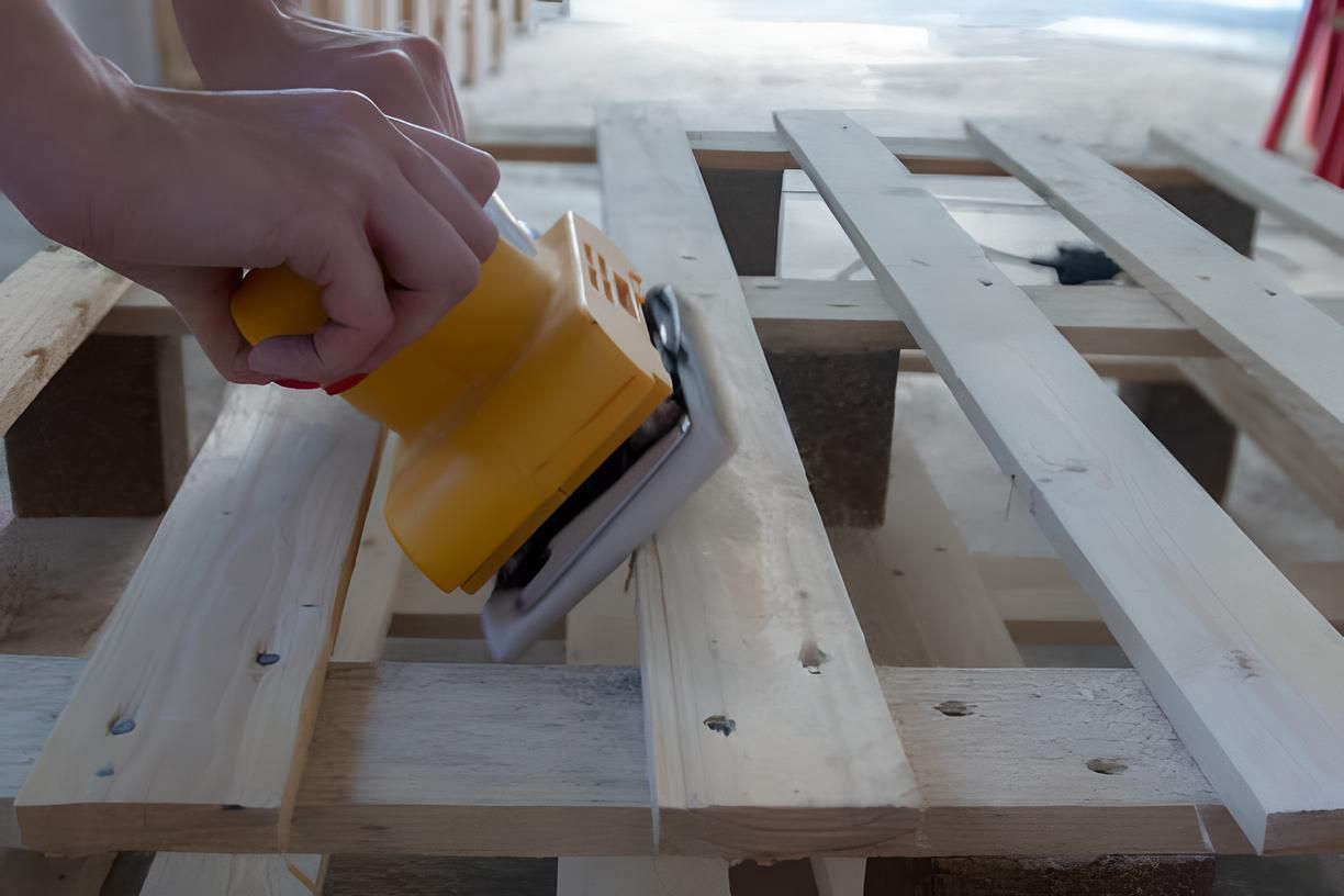 a person is sanding a wooden pallet with a yellow sander