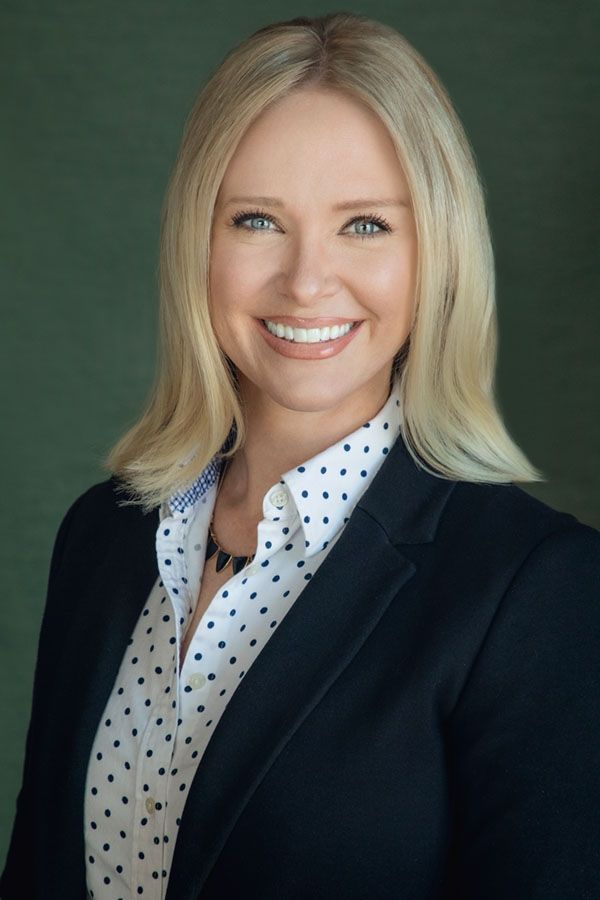 A woman is sitting at a desk with a laptop and a vase of flowers.