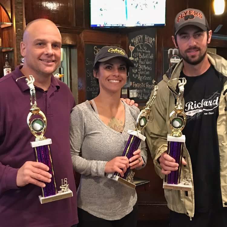 two men and a woman holding trophies in a bar