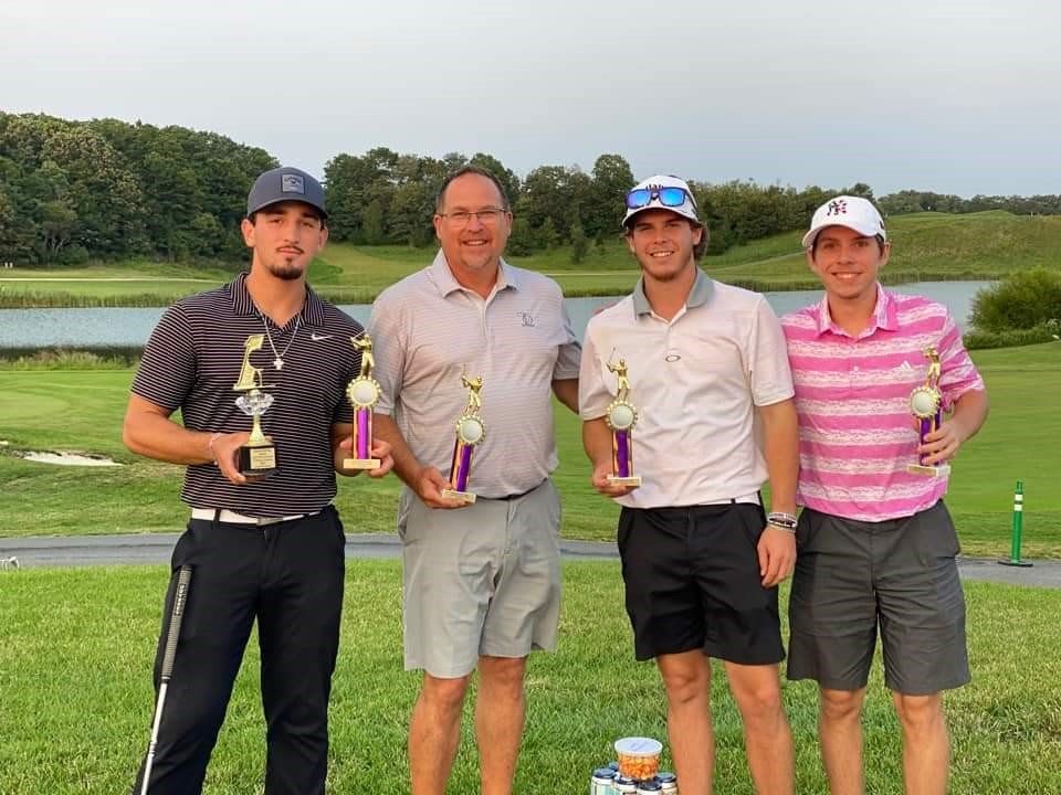 a group of men are standing on a golf course holding trophies .