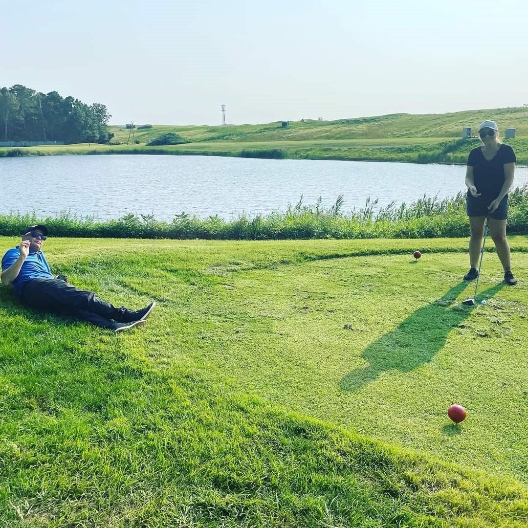 a man is laying on the grass while a woman plays golf
