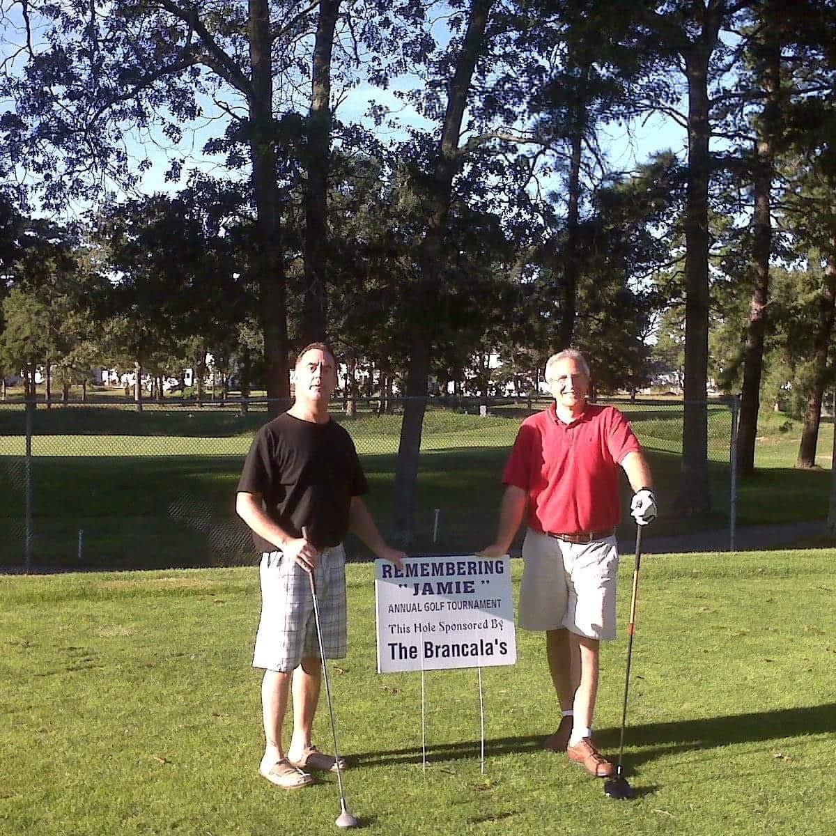 two men standing on a golf course holding golf clubs and a sign that says 