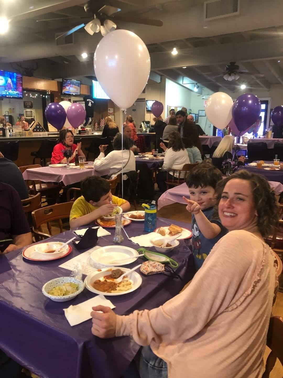 a group of people are sitting at tables with plates of food and balloons