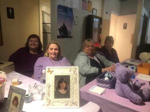 a group of women are sitting at a table with a purple teddy bear .