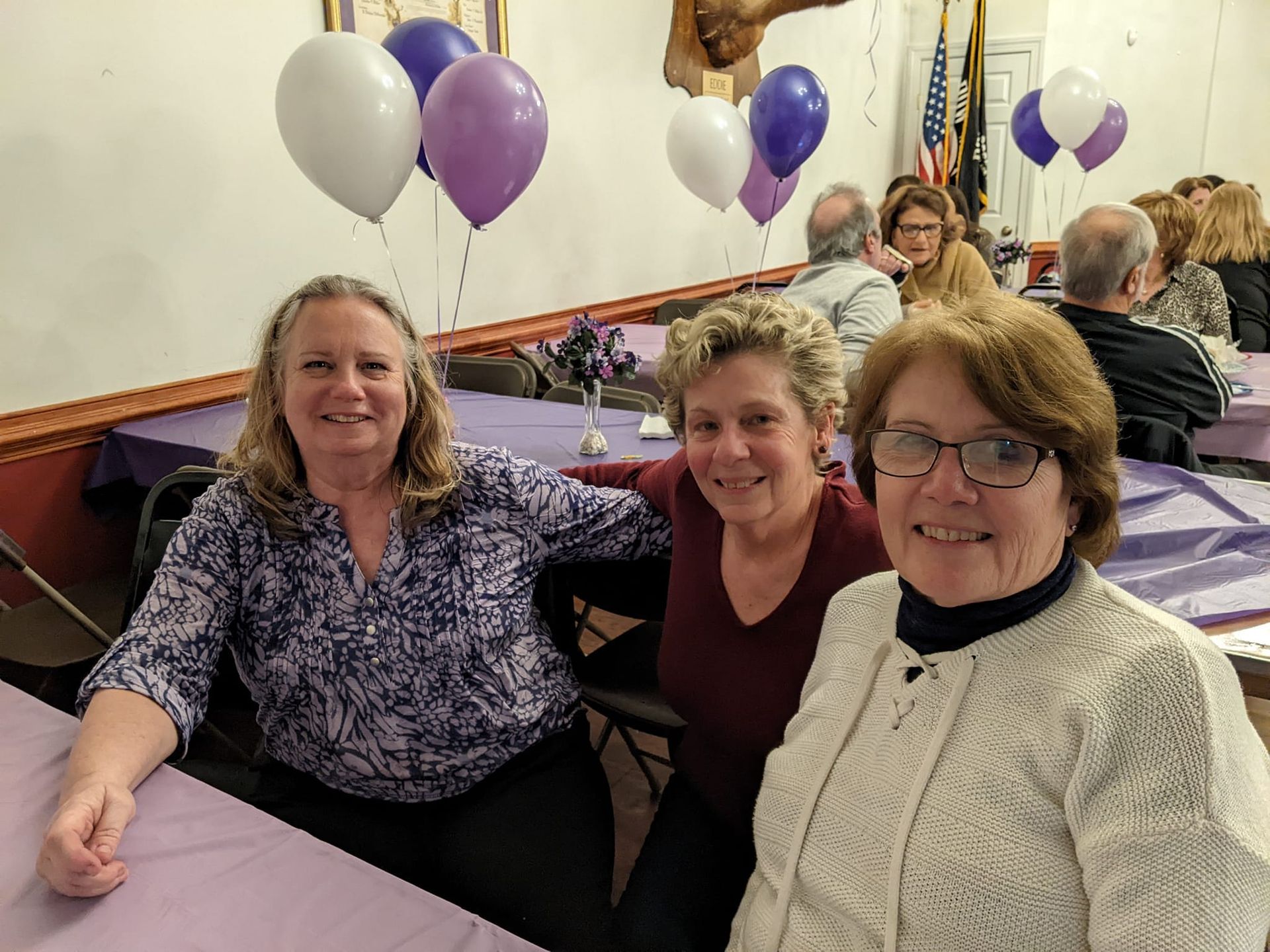 three women are posing for a picture in a room with purple and white balloons
