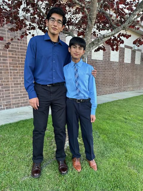 Two men are standing next to each other in front of a brick wall