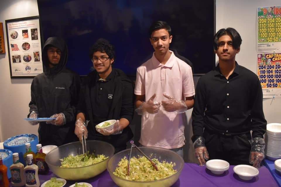 a group of young men are standing around a table with bowls of food .
