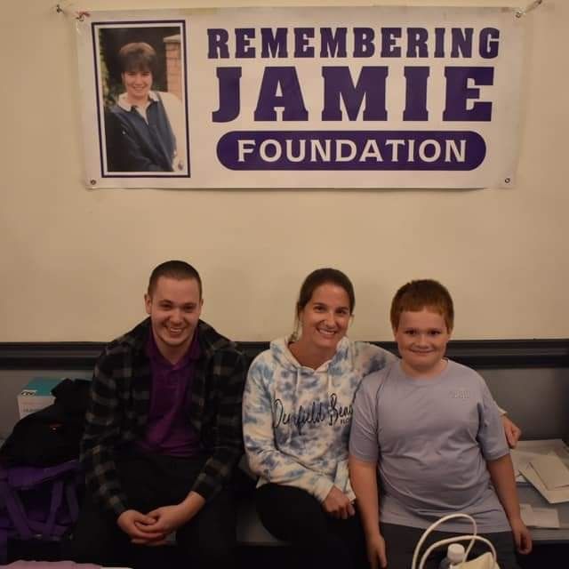 three people sitting under a banner that says remembering jamie foundation