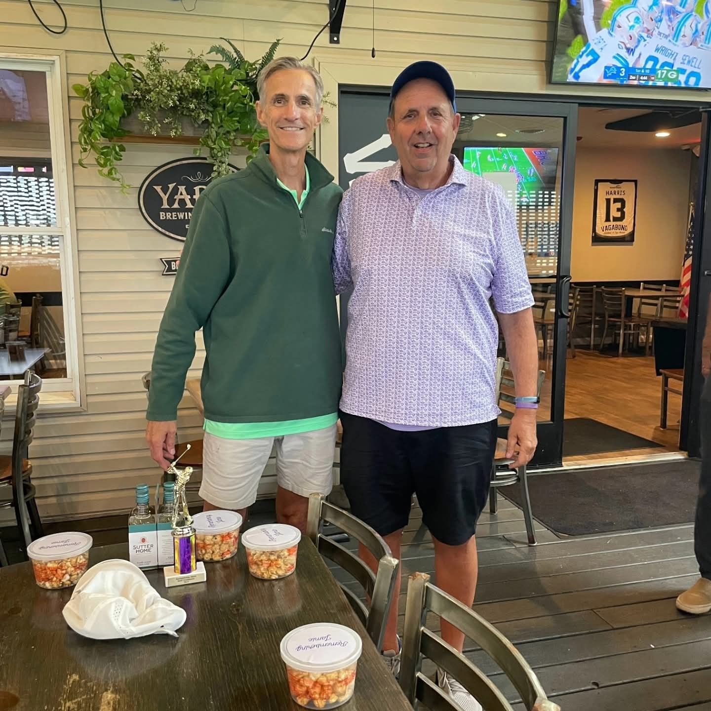 Two men pose outdoors with snacks, cups, and a trophy during the 2025 Remembering Jamie Foundation Golf Tournament at McCullough's Emerald Links Golf Course in Egg Harbor Township, New Jersey 