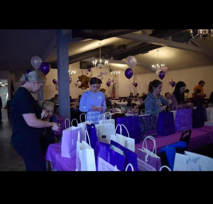 a group of people are standing around tables full of purple bags and balloons