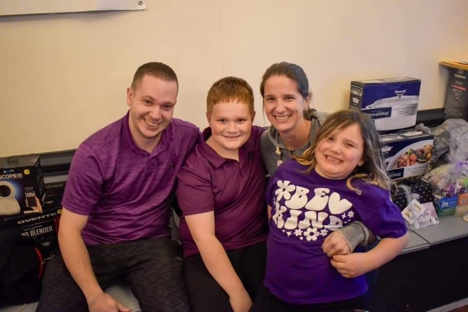 a family is posing for a picture together while wearing purple shirts .