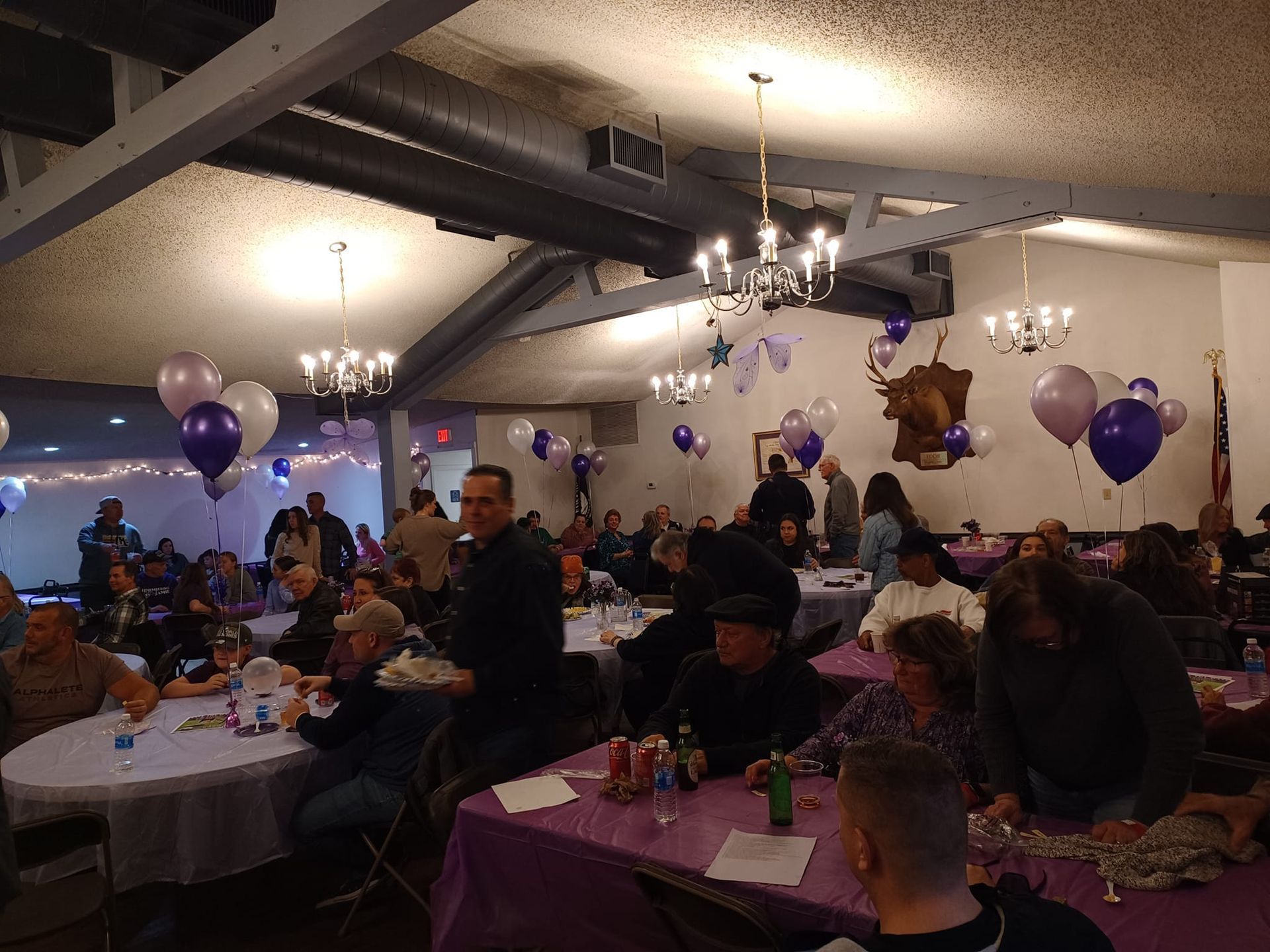 a large group of people are sitting at tables in a room decorated with purple balloons