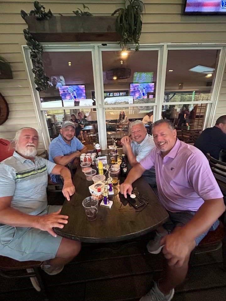 A group of men are sitting at a table in a restaurant at a golf club for the 2024 remembering jamie golf tournament