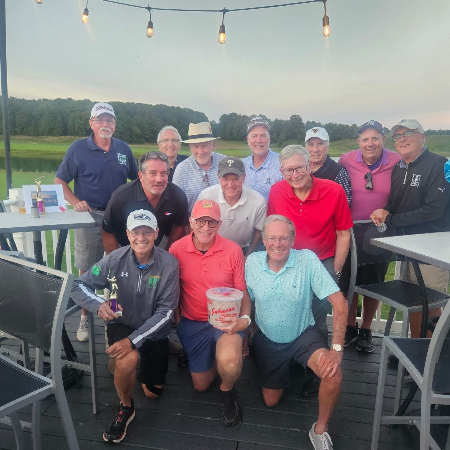A group of men posing for a picture on a deck with golf course in the background