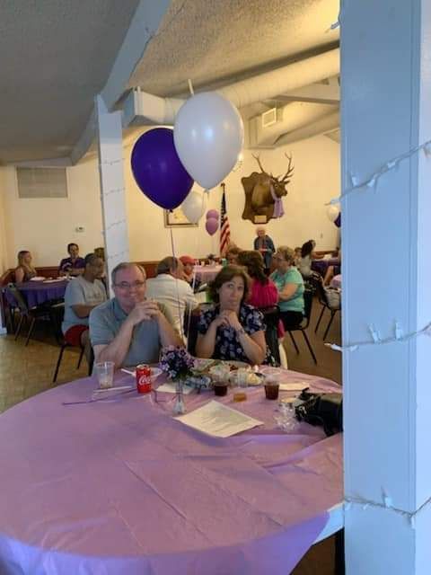 a group of people are sitting at tables in a room with balloons hanging from the ceiling .