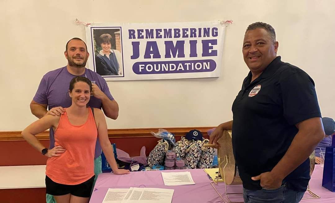 three people standing in front of a sign that says remembering jamie foundation