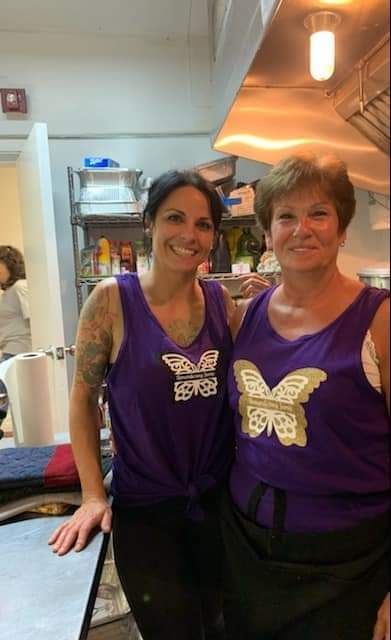 two women in purple tank tops are posing for a picture in a kitchen .