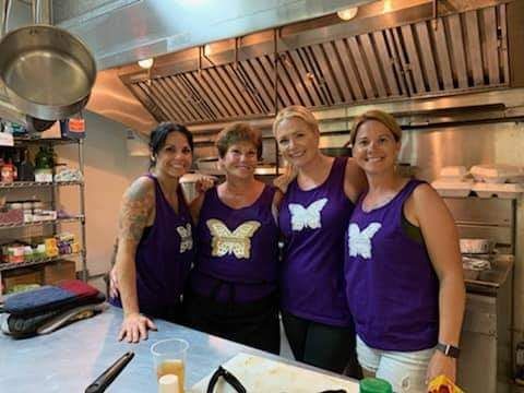 a group of women wearing purple tank tops are posing for a picture in a kitchen .