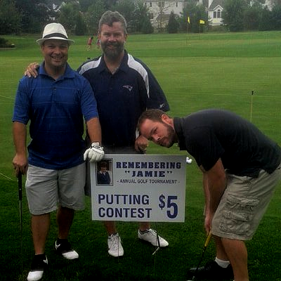 three men are standing on a golf course holding a sign that says putting contest