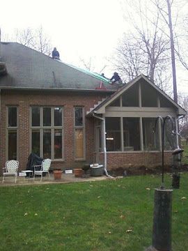 Workers on the roof of a brick house with a screen porch during a repair project.