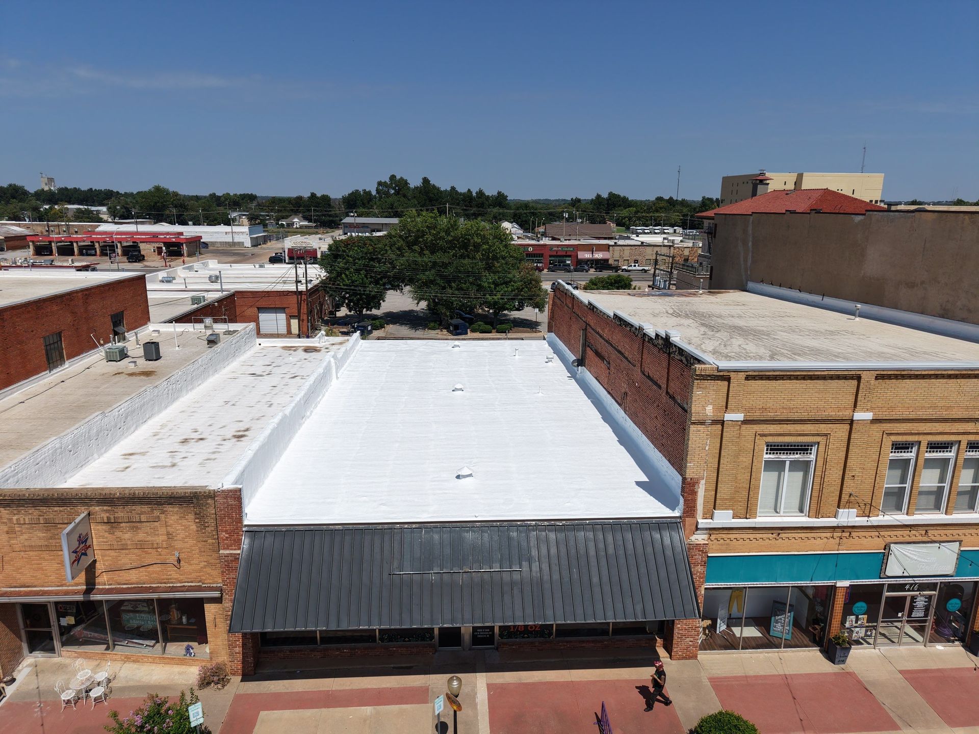 An aerial view of a downtown street with a newly white-coated flat roof between two brick storefronts.