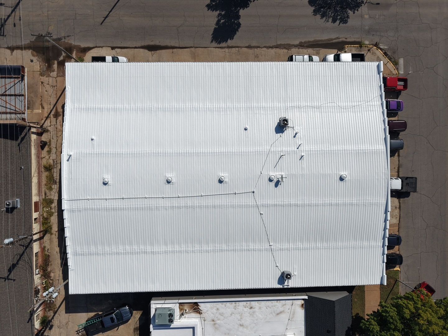 Aerial view of a white, corrugated metal industrial roof with small vents and a few people working on top.