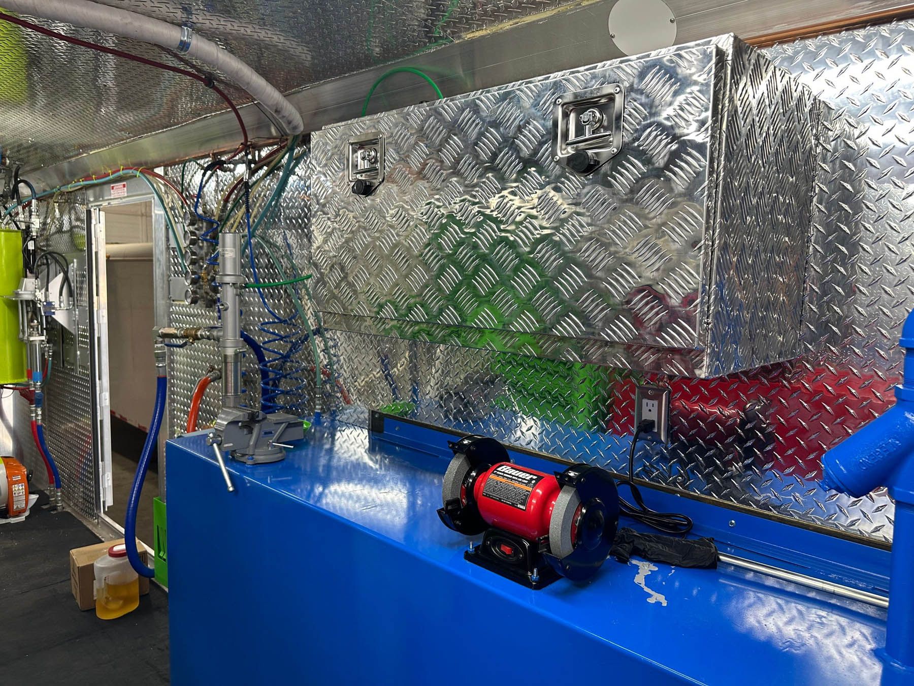 Diamond-plated metal walls inside a vehicle, with blue tanks and a red grinder visible.
