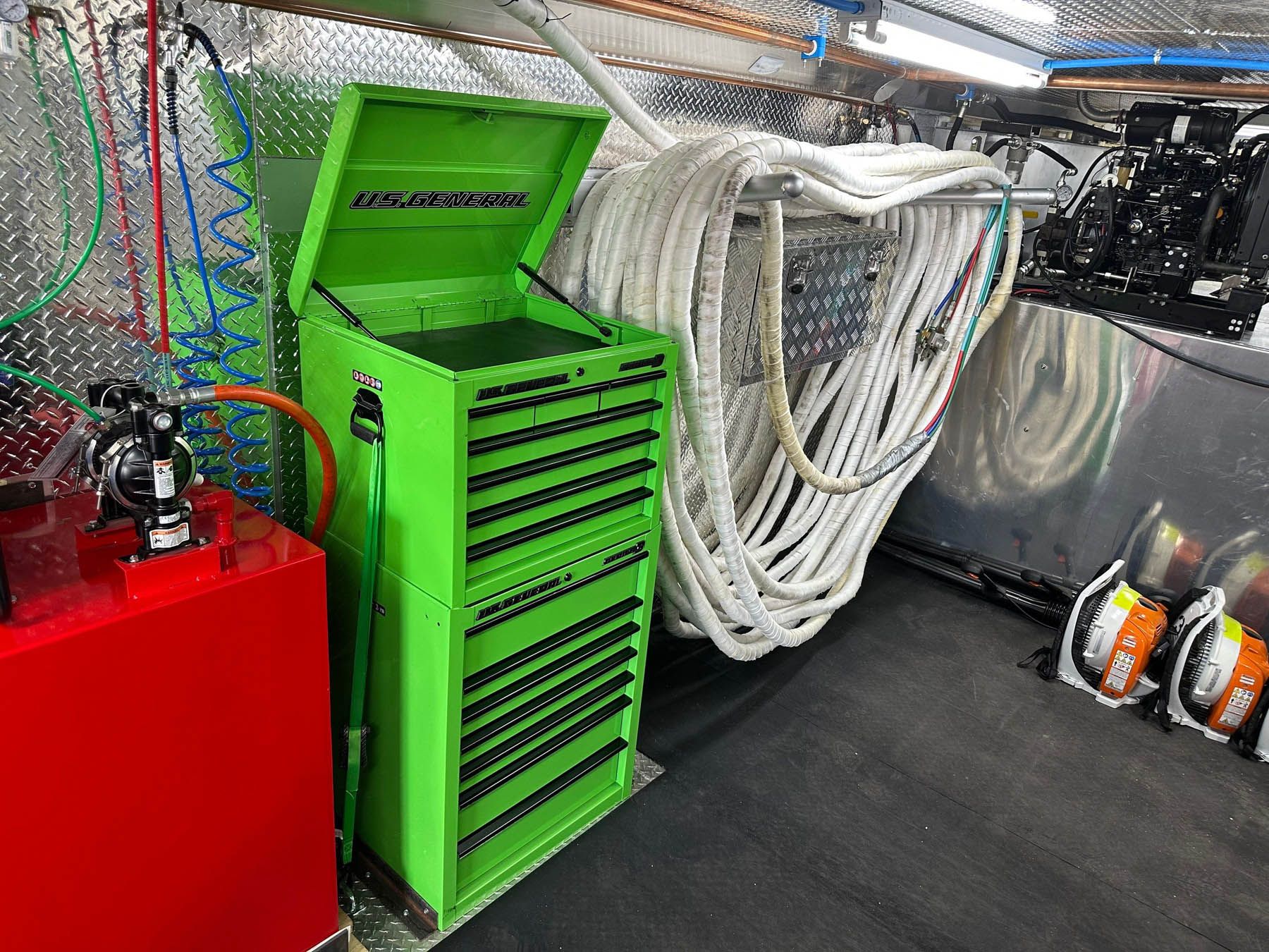 Green tool chest inside a vehicle, next to coiled white hoses and red equipment.