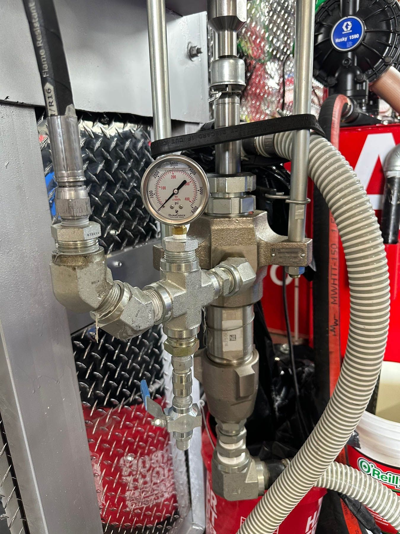 Close-up of a pressure gauge and connected metal tubes, likely part of an industrial setup, mounted on a vehicle.