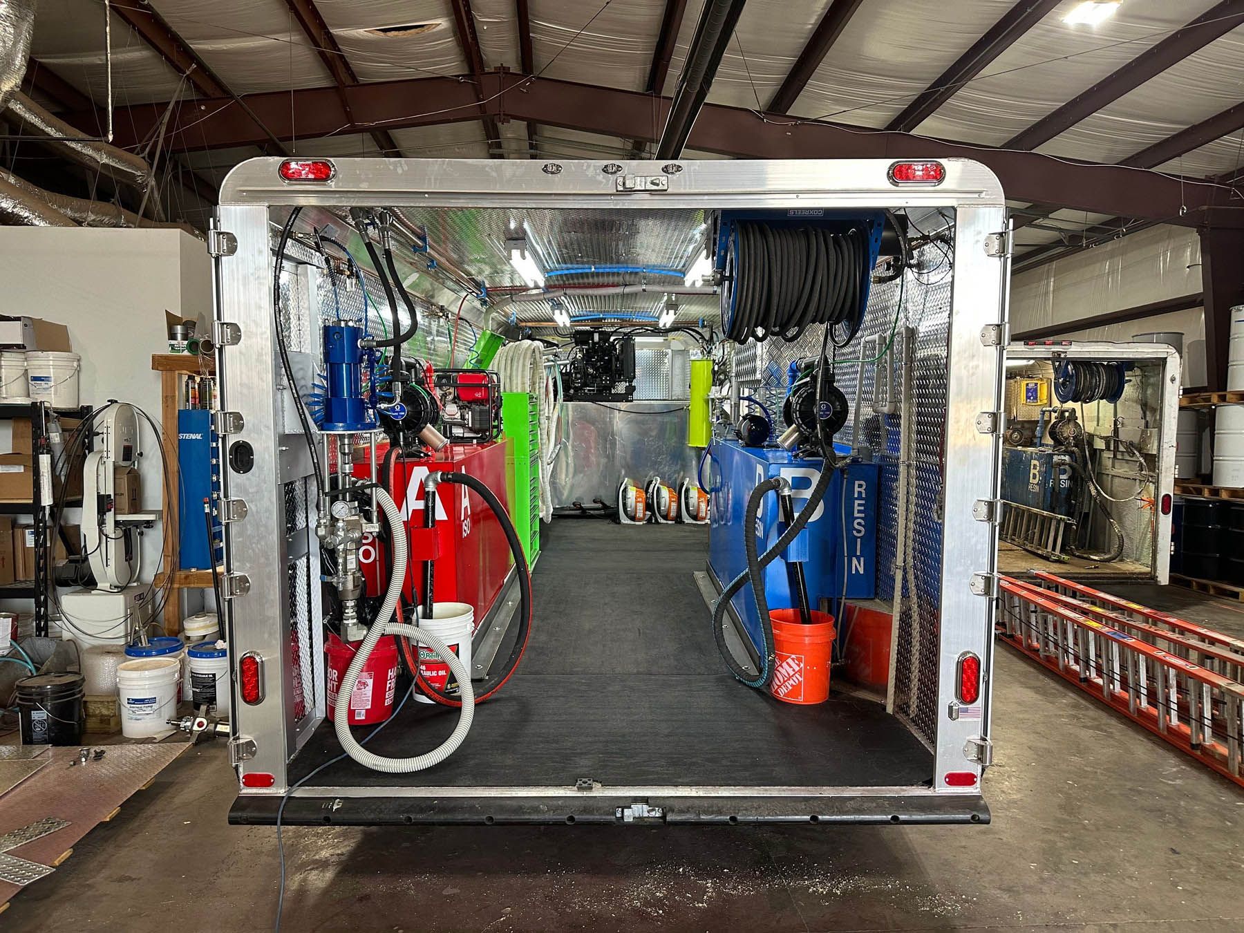Open trailer interior, with red and blue tanks, equipment, and a hose reel.