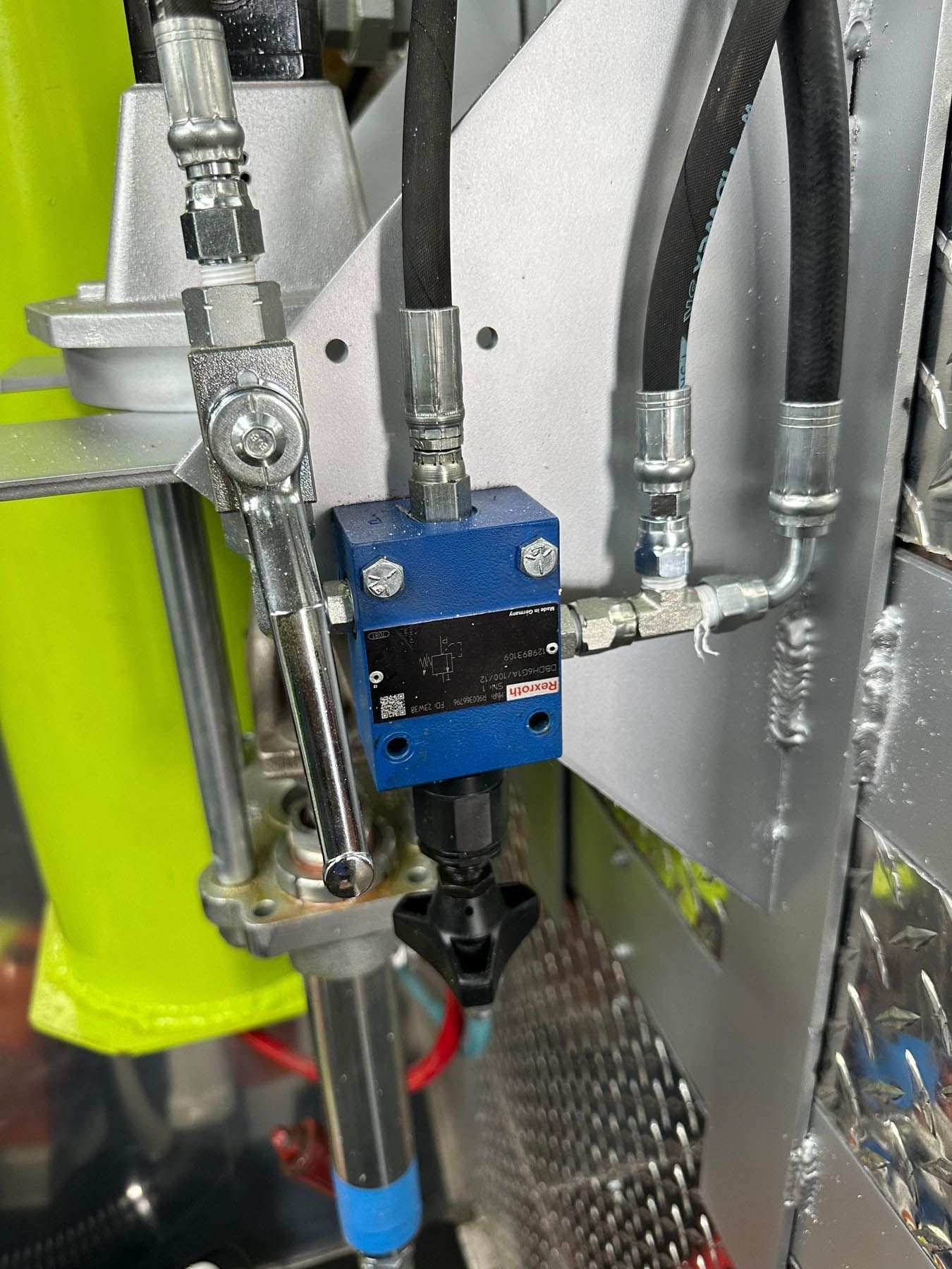 Close-up of hydraulic equipment with blue valve, black hoses, and metallic components, mounted on a metal surface.